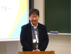 マイクの前に立つスーツの男性