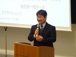 マイクの前に立つスーツの男性