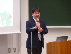 マイクを持って立つ黒いスーツの男性